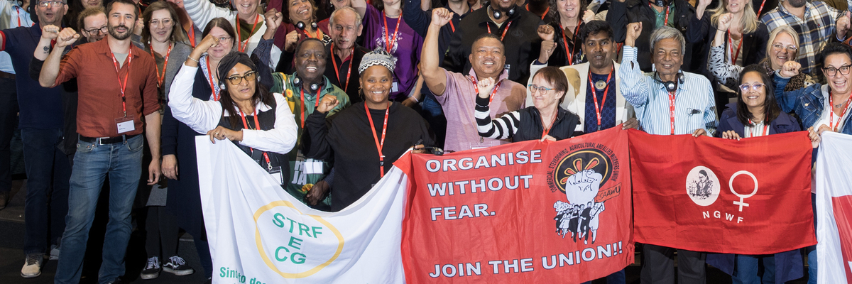 Eine Gruppe von Gewerkschafter:innen hält Banner und Schilder hoch, um ihre Botschaften "Organize without fear" während einer Versammlung zu verbreiten. 